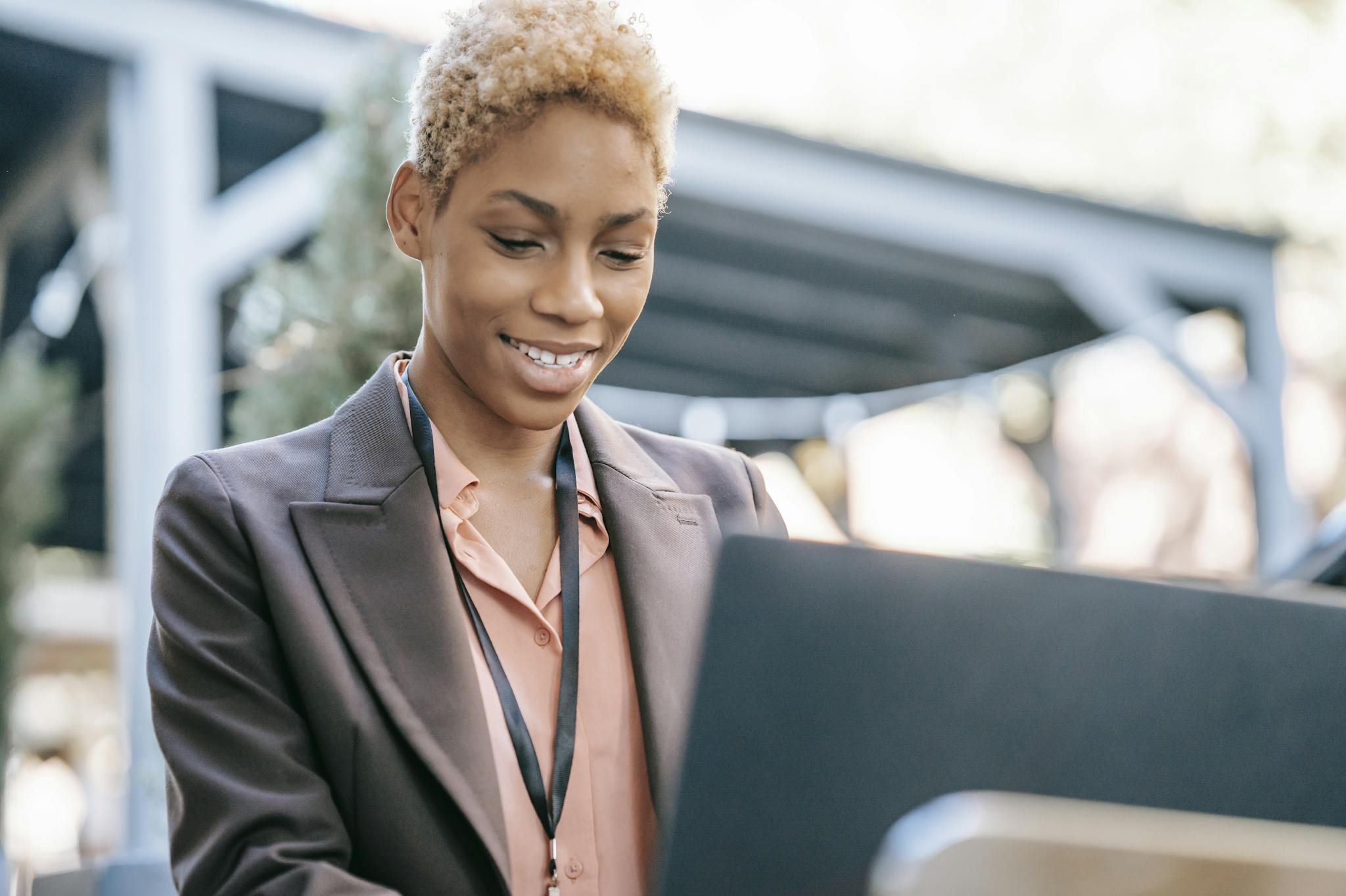 Smiling young woman in a suit using a laptop outdoors, demonstrating professional confidence.
