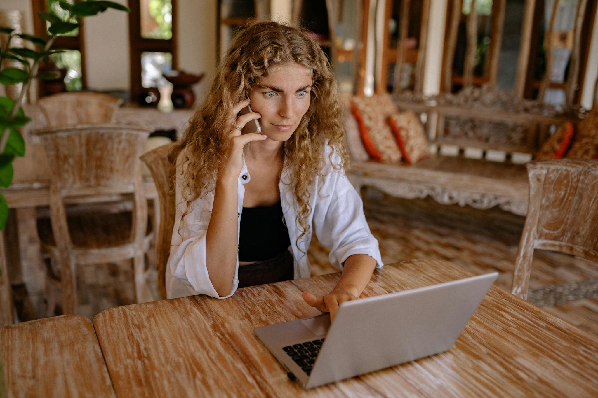 Woman working remotely on a laptop while talking on phone, capturing freelance lifestyle.
